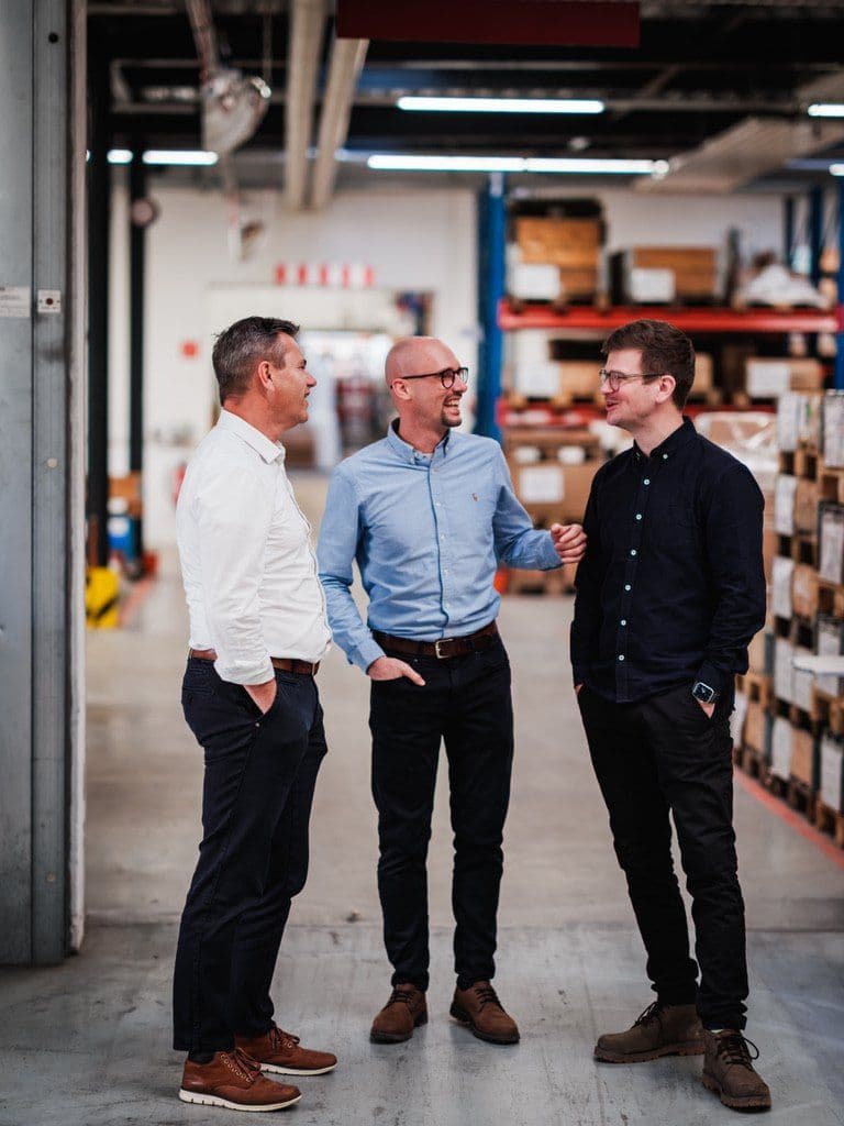 Wolfgang Auer, Christoph Reiter und Julian Kranner im Gespräch zwischen Regalen einer Lagerhalle